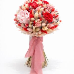 Bold preserved flower bouquet featuring red and pink roses, textured dried flowers, and soft blush ribbon on a white background
