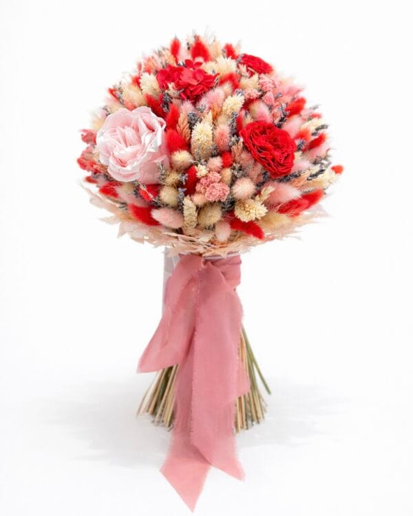 Bold preserved flower bouquet featuring red and pink roses, textured dried flowers, and soft blush ribbon on a white background