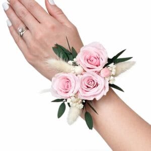 Preserved pink rose wrist corsage with eucalyptus greenery and soft dried accents worn on the wrist against a white background