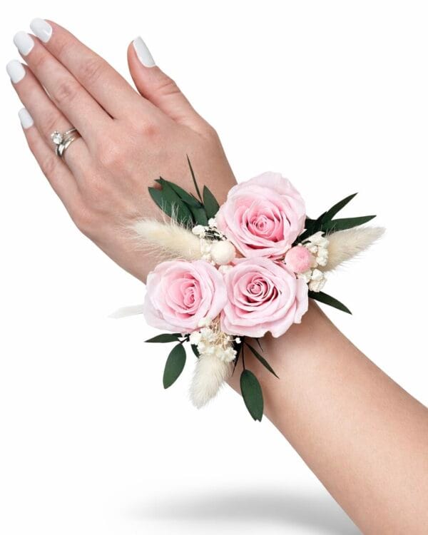 Preserved pink rose wrist corsage with eucalyptus greenery and soft dried accents worn on the wrist against a white background