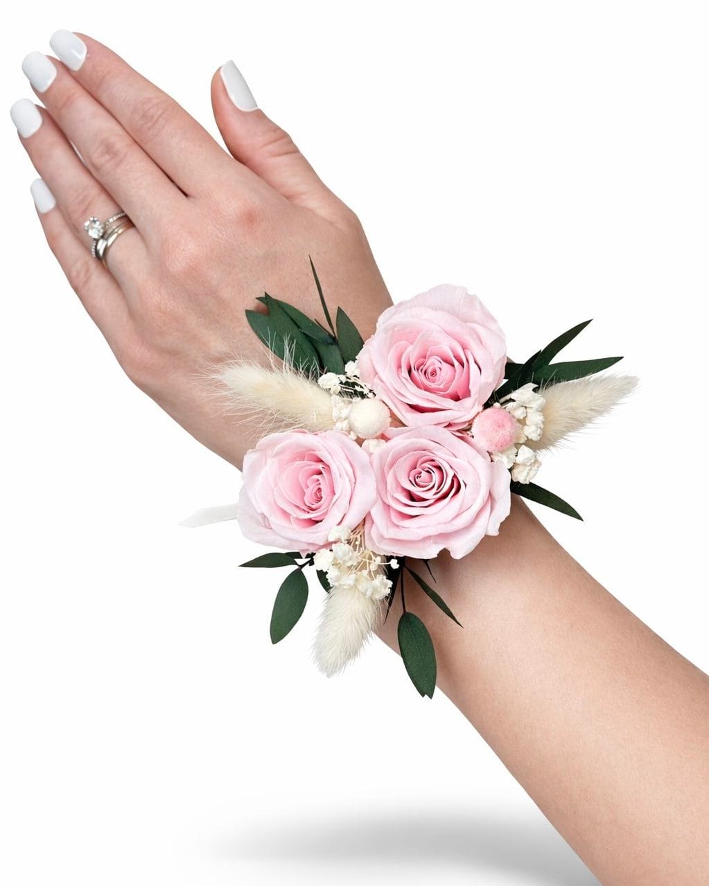 Preserved pink rose wrist corsage with eucalyptus greenery and soft dried accents worn on the wrist against a white background