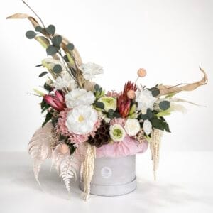 Luxury preserved flower arrangement in a hat box featuring white roses, blush hydrangea, eucalyptus, dried botanicals, and cascading textures on a white background