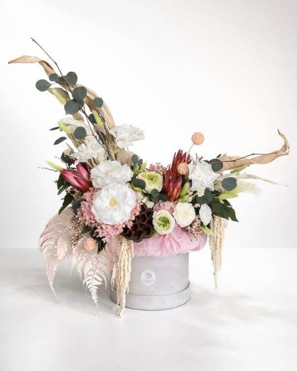 Luxury preserved flower arrangement in a hat box featuring white roses, blush hydrangea, eucalyptus, dried botanicals, and cascading textures on a white background