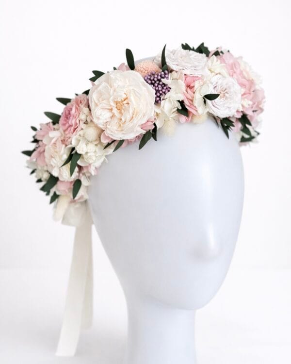Preserved flower crown with blush, ivory, and pastel flowers arranged on a mannequin head against a white background
